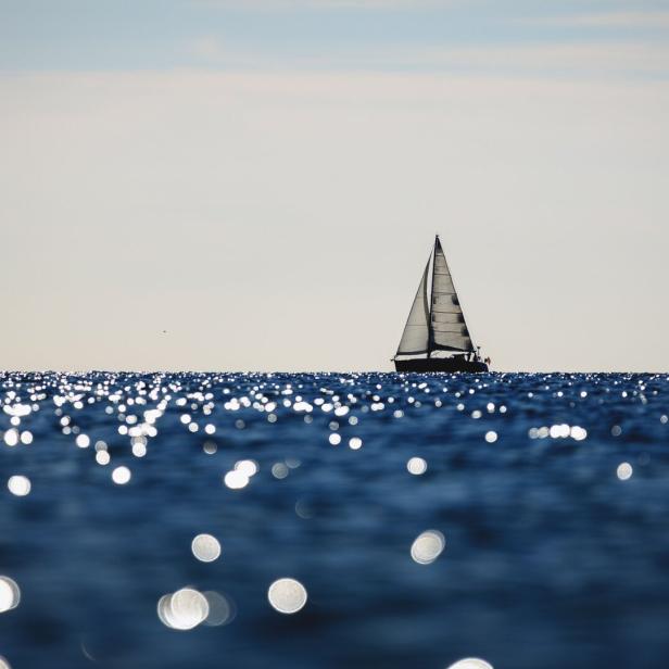 Segelboot auf glitzerndem Meer unter hellem Himmel.