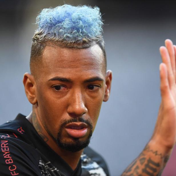Jérôme Boateng mit blau gefärbten, lockigen Haaren trägt ein schwarzes Trikot des FC Bayern München und hebt die Hand.