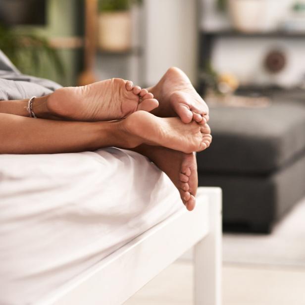 Nackte Füße und Unterschenkel liegen entspannt auf einem Bett im Wohnzimmer.