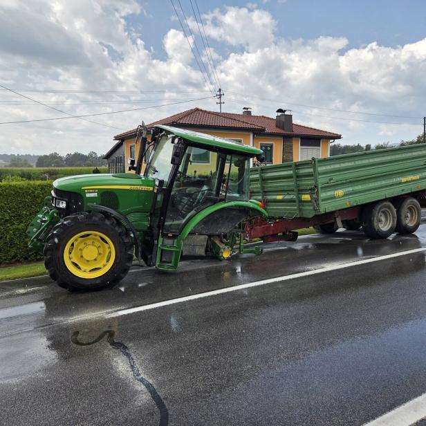 Grüner John-Deere-Traktor mit Anhänger steht auf nasser Straße vor einem Haus.