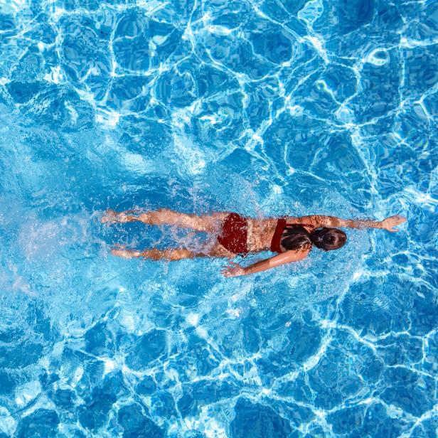 Eine Person in roter Badekleidung schwimmt in einem hellblauen Pool.