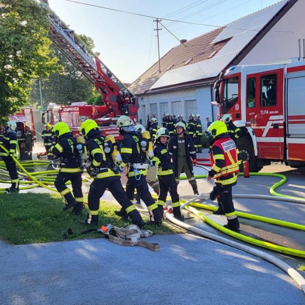 Feuerwehrleute bekämpfen einen Brand mit Schlauchleitungen und Drehleiter vor einem Haus.
