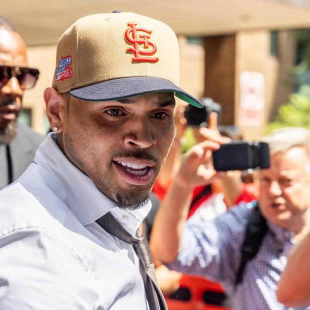 Chris Brown trägt ein weißes Hemd und eine beigefarbene St. Louis Cardinals-Kappe, während er von Fotografen umringt wird.