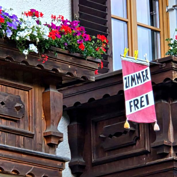 Holzfassade mit bunten Blumenkästen und einem hängenden ZIMMERT FREI-Schild.