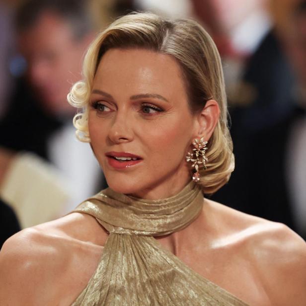 Fürstin Charlène von Monaco trägt ein goldenes Kleid und elegante Ohrringe bei einer formellen Veranstaltung.
