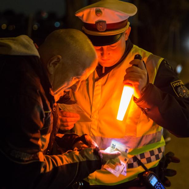 Polizist kontrolliert nachts einen Mann und beleuchtet Geldscheine mit einer Leuchte.