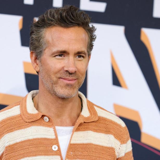 Ryan Reynolds lächelt vor einem Hintergrund mit großen Buchstaben in die Kamera.