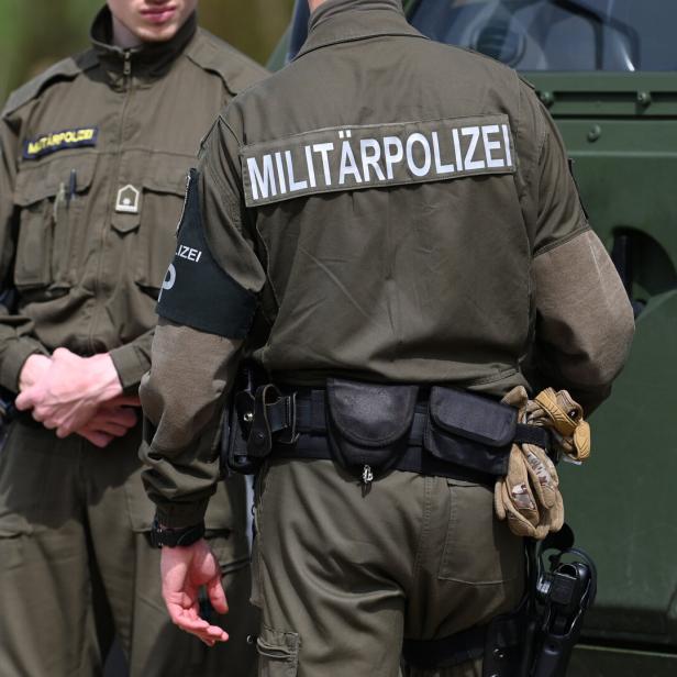Zwei Militärpolizisten in Uniform stehen vor einem grünen Militärfahrzeug.