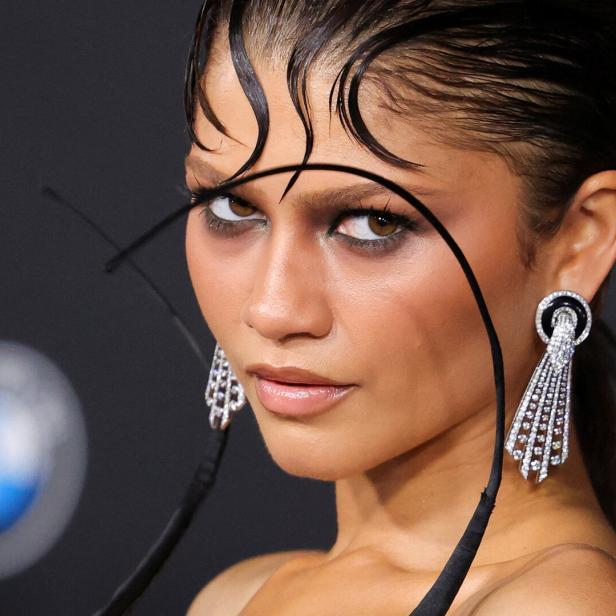 Zendaya blickt mit nassem Haar-Styling und auffälligen Ohrringen vor einem dunklen Hintergrund mit BMW-Logo in die Kamera.