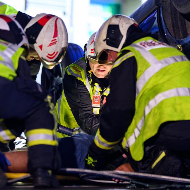 Rettungskräfte in Helmen und Warnwesten arbeiten dicht gedrängt an einer eingeklemmten Person.