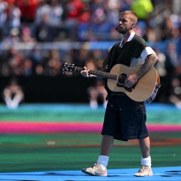 Justin Bieber spielt vor einem großen Publikum auf einer bunten Bühne eine Akustikgitarre.