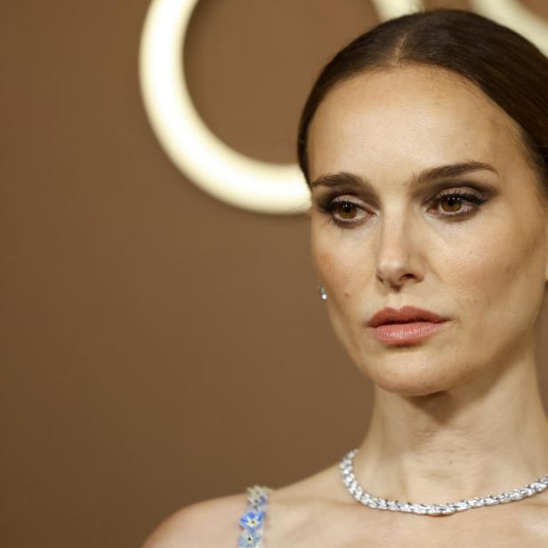 Natalie Portman trägt ein elegantes Collier und ein verziertes Kleid vor einem goldfarbenen Hintergrund.