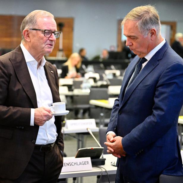 Zwei Männer im Anzug sprechen in einem Konferenzsaal, einer hält eine Kaffeetasse.