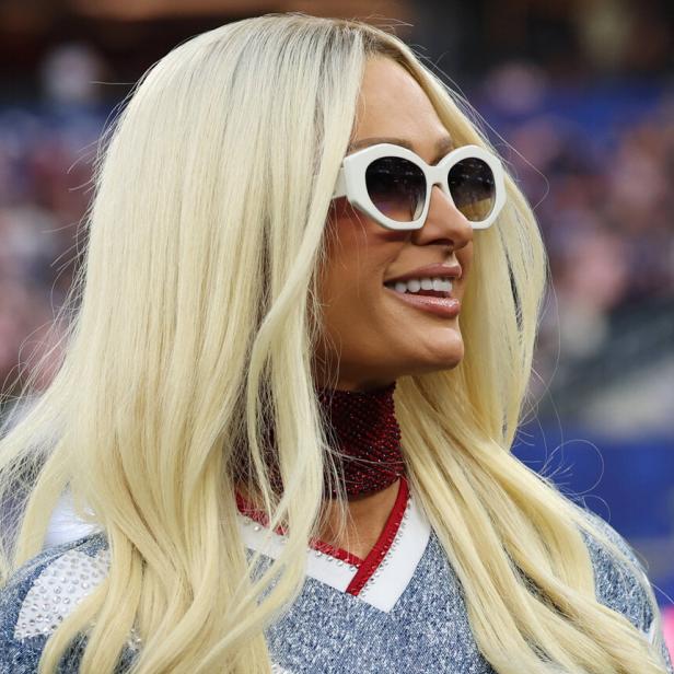 Paris Hilton trägt langes blondes Haar, eine weiße Sonnenbrille und ein glitzerndes Oberteil.