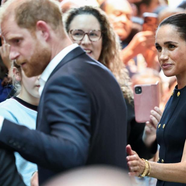 Prinz Harry und Meghan Markle inmitten einer Menschenmenge, die sie mit Smartphones fotografiert.