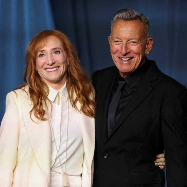 Patti Scialfa und Bruce Springsteen lächeln gemeinsam vor einem blauen Hintergrund in die Kamera.