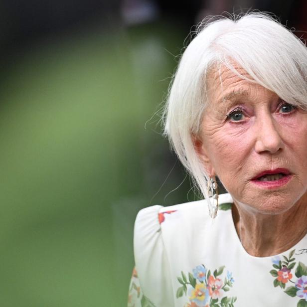 Helen Mirren mit weißem Haar und einem floralen Kleid blickt aufmerksam zur Seite.