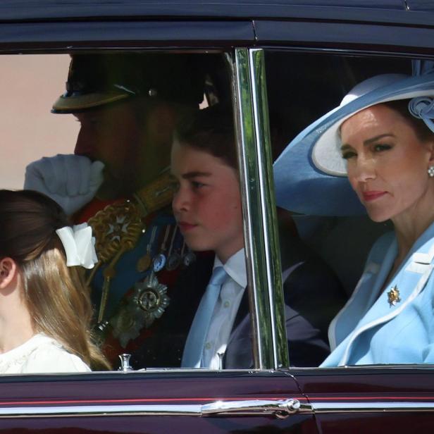 Prinzessin Catherine, Prinz George und Prinzessin Charlotte sitzen in einer Kutsche oder einem Auto, begleitet von einem uniformierten Offizier.