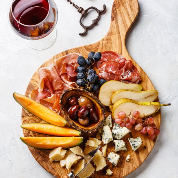 Ein Holzbrett mit Schinken und Käse garniert mit Melone und Birne