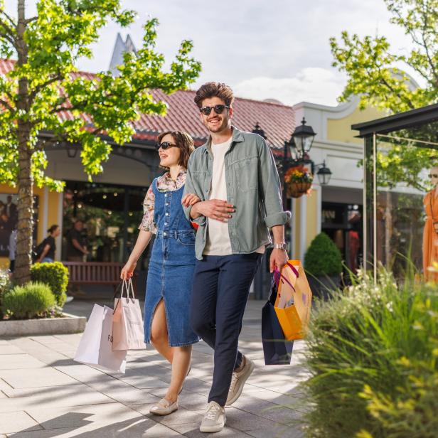 Ein Paar läuft Arm in Arm durch ein Shoppingcenter, mit Einkaufstaschen in der Hand. 