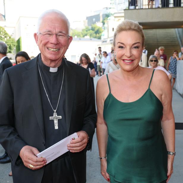 Ein lächelnder Geistlicher mit Kreuz und eine Frau im grünen Kleid stehen bei einer Veranstaltung im Freien.