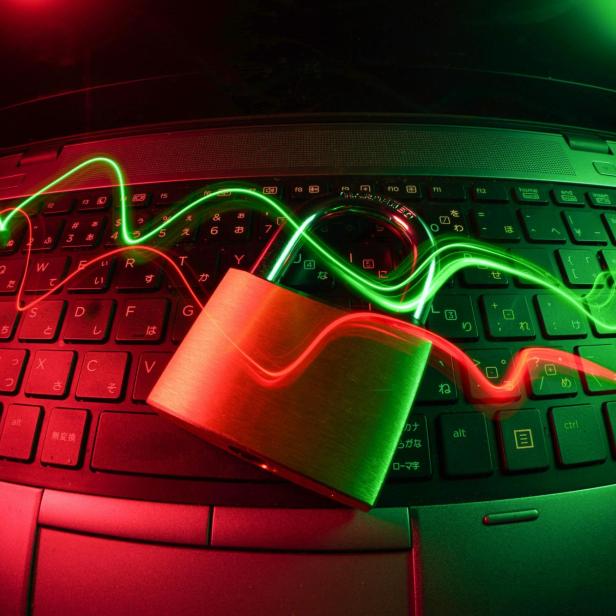 Ein Vorhängeschloss liegt auf einer Laptop-Tastatur, darüber verlaufen rote und grüne Lichtspuren als Symbol für Cyberangriffe und digitale Abwehr.