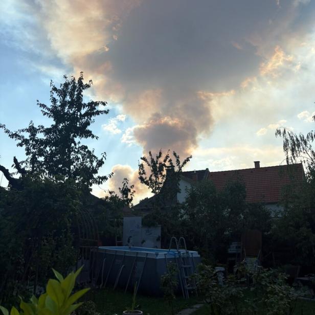 Große, von der Sonne goldgeränderte Wolke über einem Garten mit Pool und Hausdächern.