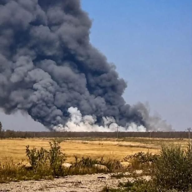 Dicker schwarzer Rauch steigt hinter einer trockenen Landschaft in den Himmel.