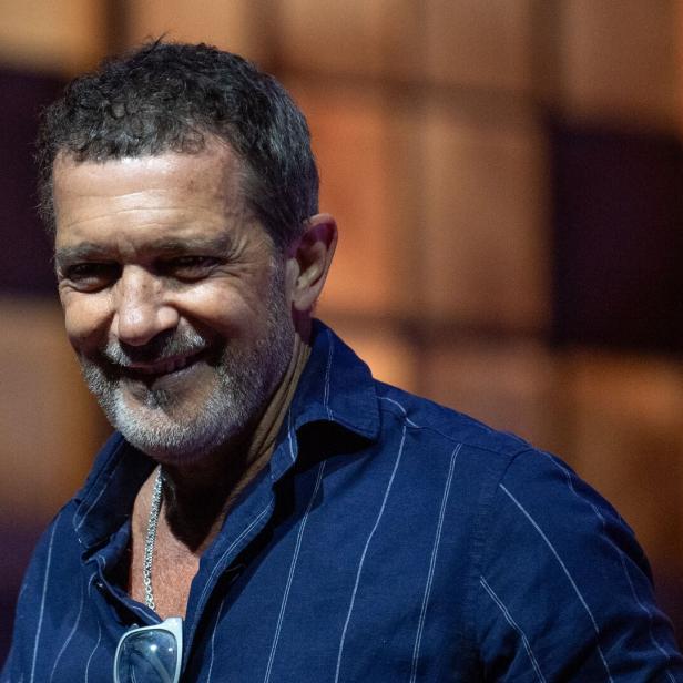 Antonio Banderas lächelt in einem dunkelblauen, gestreiften Hemd vor einem unscharfen Hintergrund.