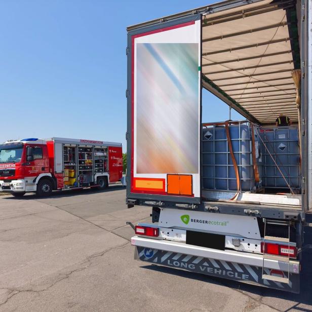 Feuerwehrwagen neben einem offenen Lkw mit IBC-Behältern an einer Landstraße.