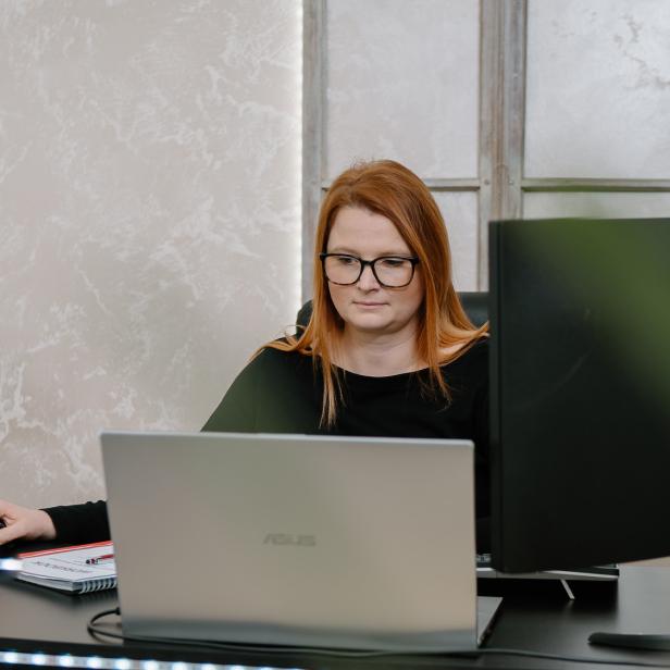 Eine rothaarige Frau sitzt an einem Laptop an einem Schreibtisch 
