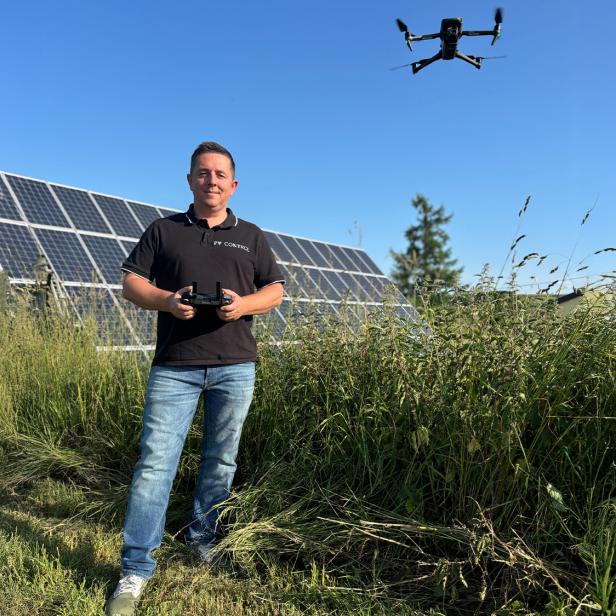 Mann steuert eine Drohne vor Solarmodulen.