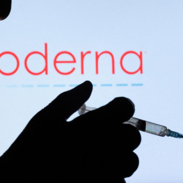 FILE PHOTO: People pose with syringe with needle in front of displayed Moderna logo