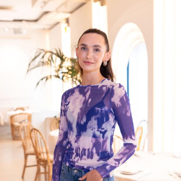Anna Adamyan posiert in einem hellen Restaurant mit lila Oberteil und Jeans.