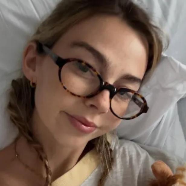Sydney Towle mit einer Brille auf der Nase liegt in einem Bett