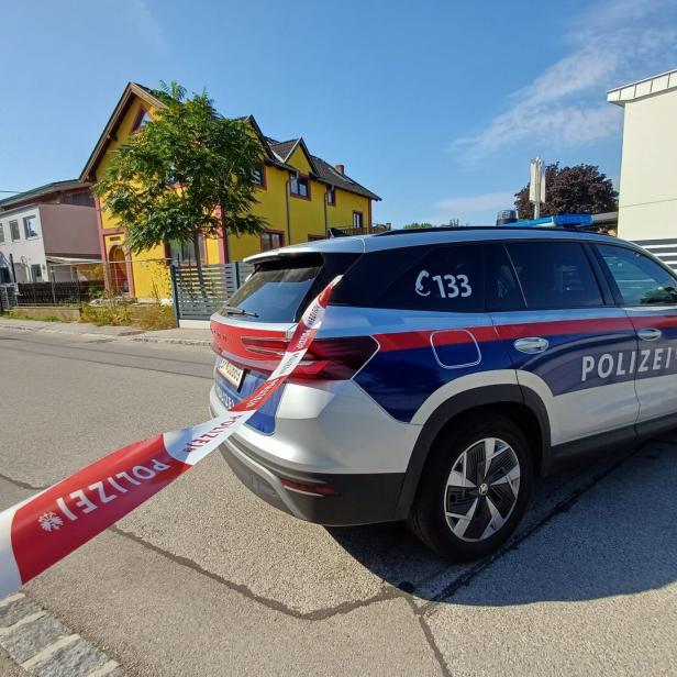 Polizeiwagen in Absperrband vor Wohnhäusern auf einer Straße.