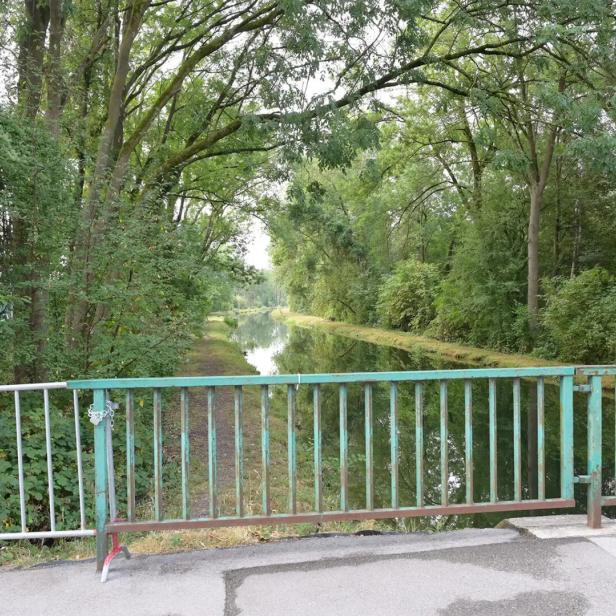 Bewaldeter Kanal hinter einer gesperrten Brücke mit Fußgängerverbotsschild.