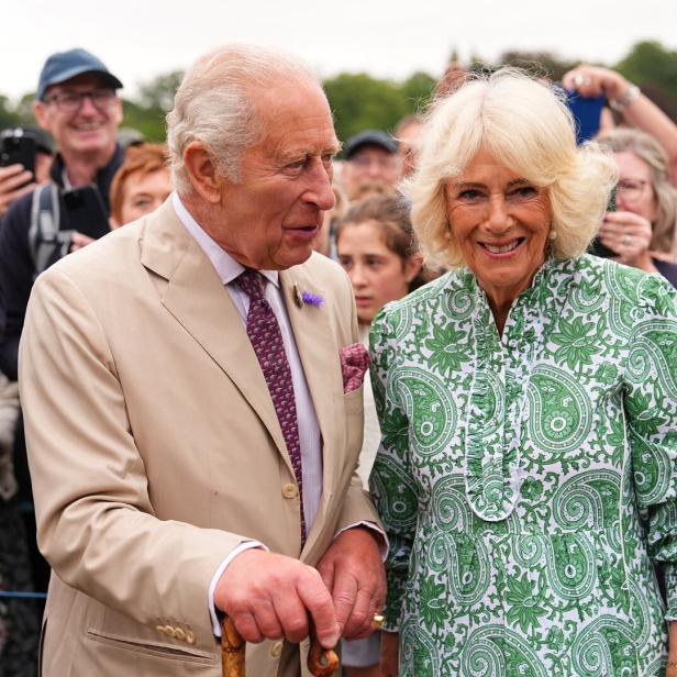 König Charles III. und Königin Camilla lächeln bei einem öffentlichen Auftritt in eine Menschenmenge.