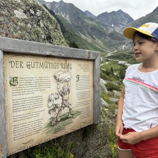 Ein Mädchen liest vor einer Bergkulisse eine Informationstafel über den „Gutmütigen Riesen“ am Pitztaler Sagenweg.