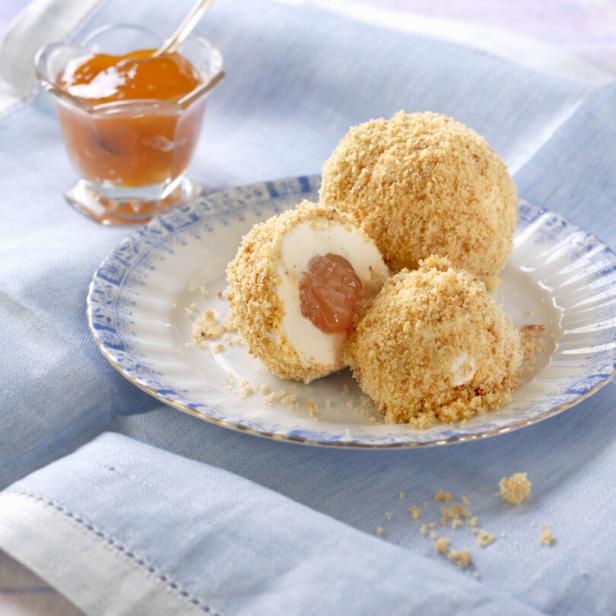 Marillenknödel mit Bröseln auf einem Teller, daneben ein kleines Glas mit Aprikosenkonfitüre auf einem blauen Tuch.