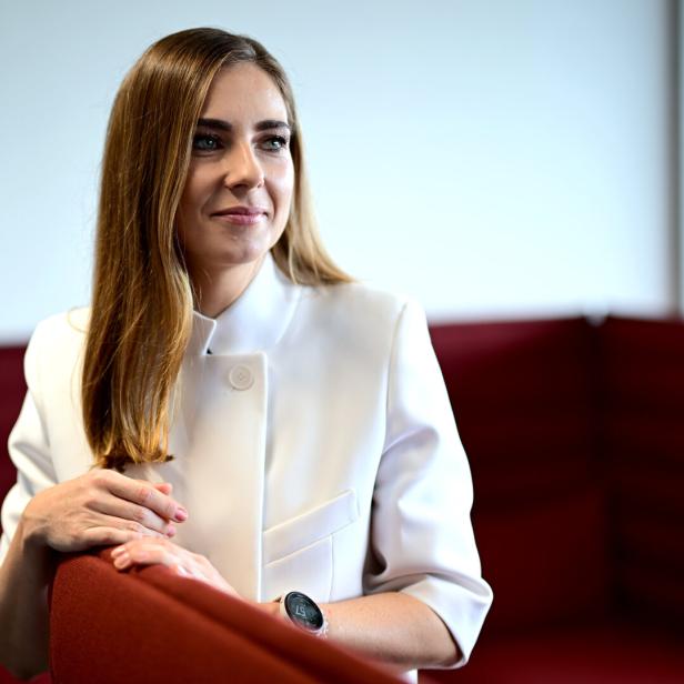 Simone Stribl in weißer Jacke sitzt an einem roten Stuhl und blickt nach rechts.
