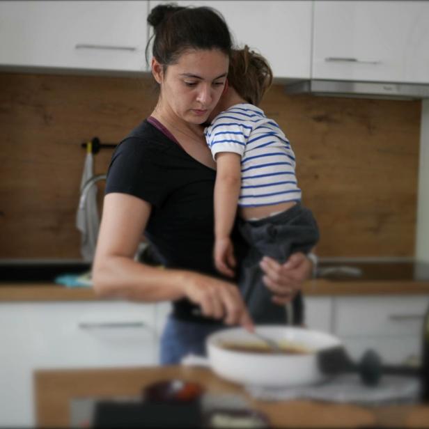 Mother holding son while cooking mom multi-tasking at home preparing food