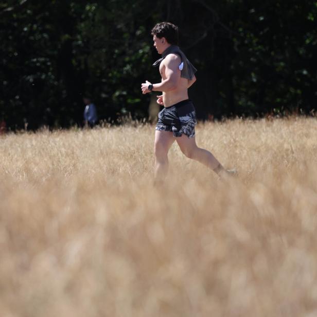 Ein barfüßiger Mann joggt durch ein trockenes Grasfeld vor dunklem Wald.