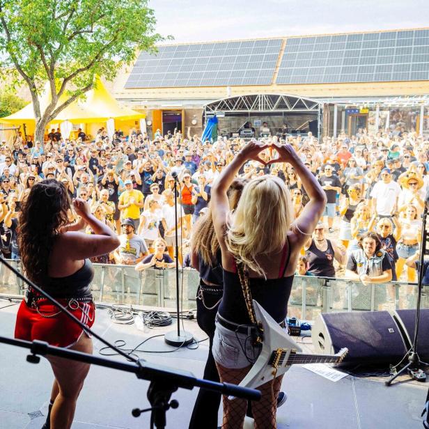 Band auf einer Open-Air-Bühne vor jubelnder Menschenmenge, die Sängerinnen begrüßen das Publikum.