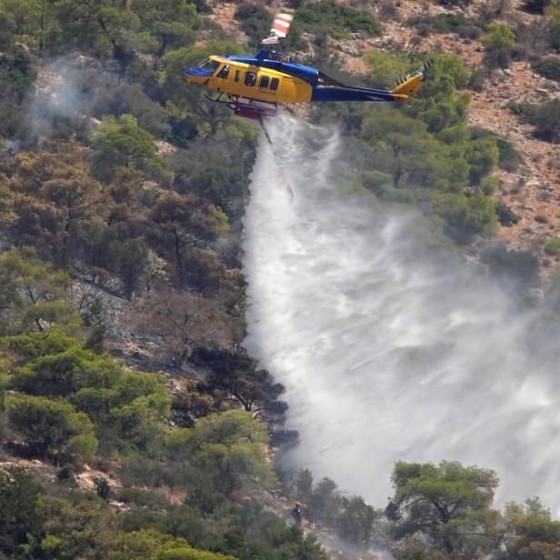 Ein Hubschrauber löscht einen Waldbrand und lässt Wasser auf den bewaldeten Hang nieder.