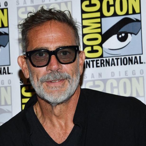 Jeffrey Dean Morgan mit Brille und grauem Bart vor einer Comic-Con-Hintergrundwand.