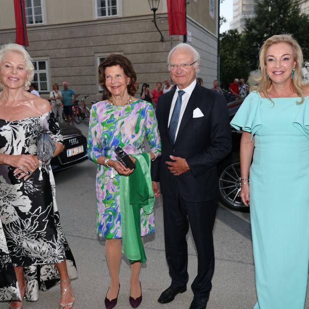 Königin Silvia und König Carl XVI. Gustaf von Schweden posieren gemeinsam mit zwei elegant gekleideten Frauen vor einem Gebäude.