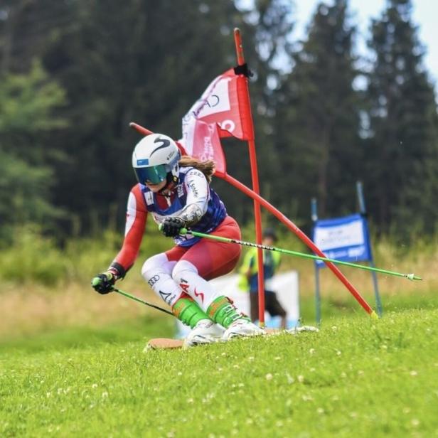 Skirennfahrerin in Rennhaltung durchfährt einen Slalom zwischen Toren auf einer Wiese.