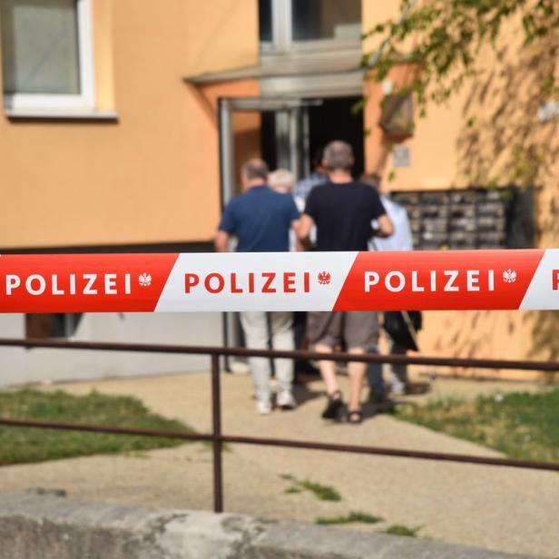 Polizeisperre vor einem Wohnhaus, dahinter gehen Menschen zum Eingang.