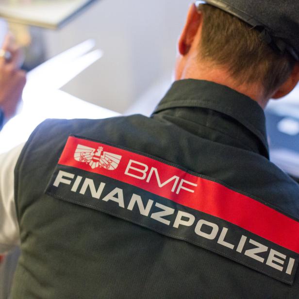 Ein Finanzpolizist mit erhobener Hand in Uniform mit der Aufschrift BMF und FINANZPOLIZEI.